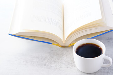 ページを開いた本（洋書）とコーヒーの入ったコーヒーカップで、コーヒーを飲みながら読書を楽しむイメージ
