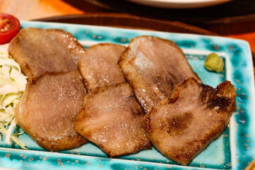 close up of Japanese sliced grilled ox beef tongue on a blush green plate with cabbage and cherry tomato on the side