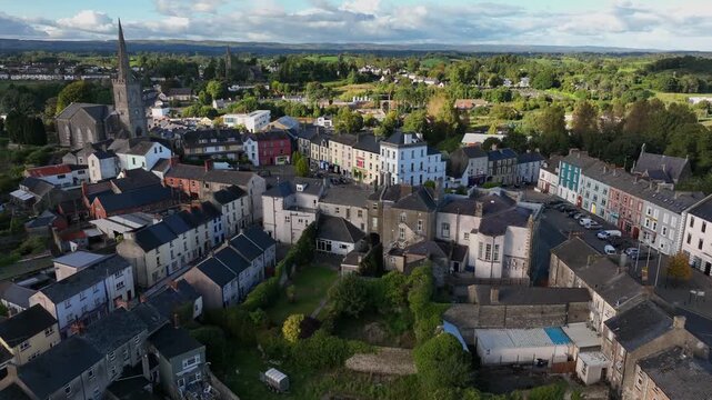 Clones Town, County Monaghan, Ireland, April 2023. Drone ascends gradually over the buildings surrounding the Diamond in the center of town as warm sunlight graces the rooftops and trees.