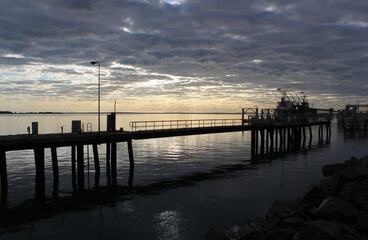 Obraz premium Seaside pier extending over the ocean with a cloudy sky at dawn