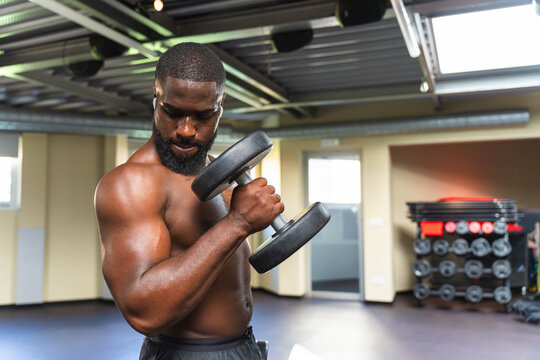 Black man with muscular body working upper body with dumbbells