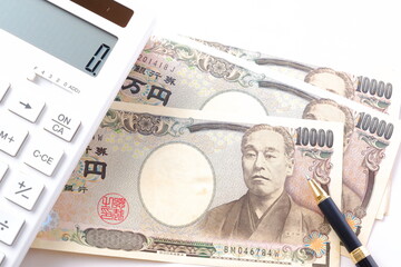 福沢諭吉の肖像の一万円紙幣と電卓、ペン
