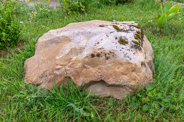 Fototapeta premium Large granite stone lies on the grass in the garden. Detailed photo of big granite stone. 