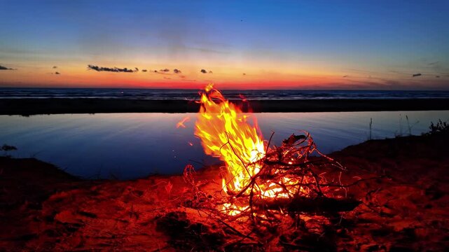 Motion video of blazing bonfire at shore of a lake in Irbes ieteka, Kempings, Latvia during sunset.