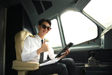 Confident professional airline pilot showing thumb up while sitting in the cockpit of an aircraft