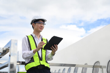 Professional aviation engineer using digital tablet while standing on staircase or platform near...