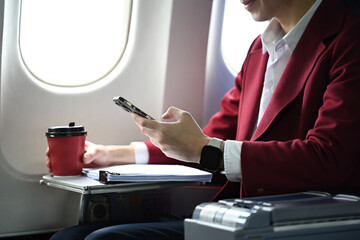 Businessman holding a paper cup of coffee and using mobile phone inside airplane