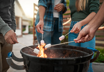 Flame, hands and people roasting marshmallows in backyard for social event, gathering or hang out. Grill, fire and group of friends toasting, burning or melting sweet treat for smores snack outdoor.