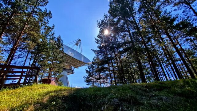 Low angle view capturing RT-32 telescope surrounded with tall trees in Irbene, Latvia during daytime.
