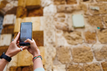 A young woman takes photos of sights on her phone. A girl visits the old city of Arco-Israel.  Travel and vacation lifestyle concept