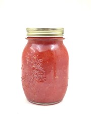 Photo of a glass jar filled with homemade tomato sauce, isolated on white background.
