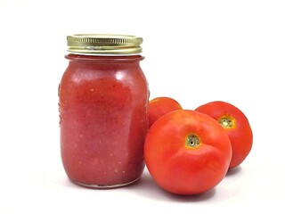 Photo of two glass jars filled with homemade tomato sauce sits alongside three fresh tomatoes, highlighting the sauce’s natural ingredients, isolated on white background.