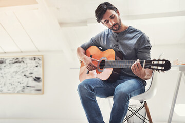 Obraz premium Playing, home and man with guitar for performance, music practice and rehearsal in living room. Entertainment, musician and person with musical instrument for audio, creative talent and writing song