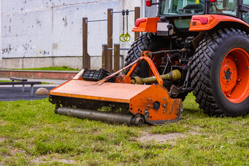 Close up of large orange tractor moving green farmers pasture. Tractor with a grass mower in the city. Mowing the silage