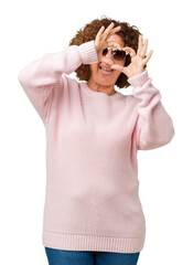 Beautiful middle ager senior woman wearing pink sweater and sunglasses over isolated background Doing heart shape with hand and fingers smiling looking through sign