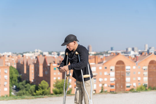 disabled man using his smartphone while walking with his crutches