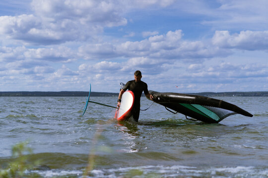 A man athlete comes out of the water with wingfoil equipment.