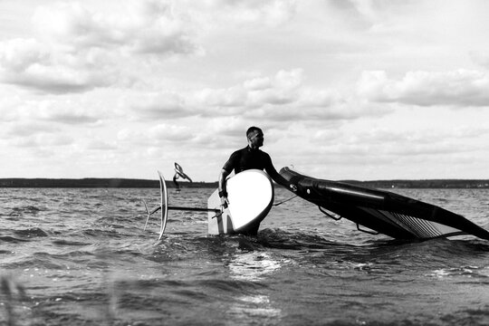 A man athlete comes out of the water with wingfoil equipment.