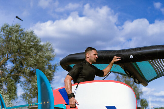A man athlete comes out of the water with wingfoil equipment.