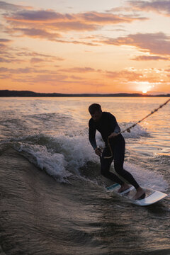 Man wake surfing in lake against sunset sky.