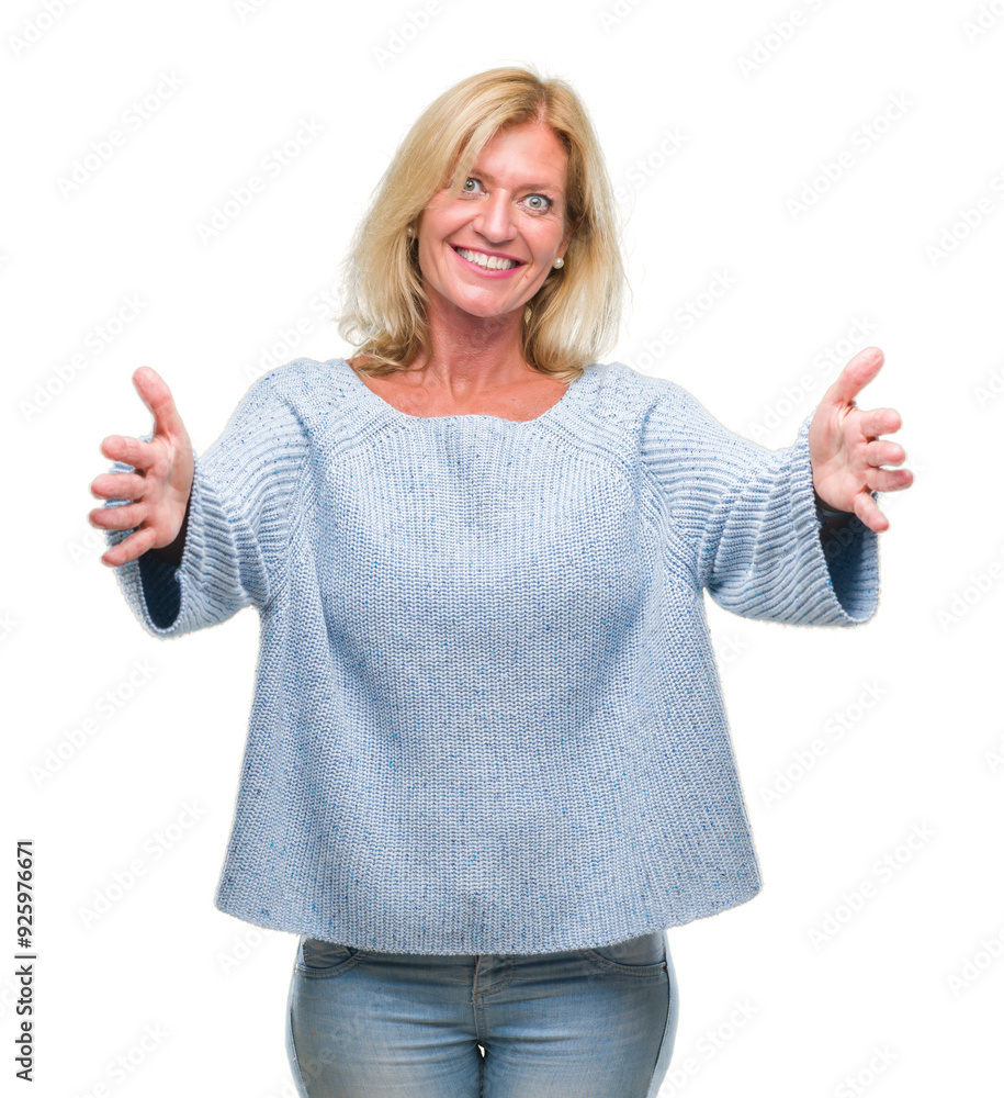 Wall mural Middle age blonde woman wearing winter sweater over isolated background looking at the camera smiling with open arms for hug. Cheerful expression embracing happiness.