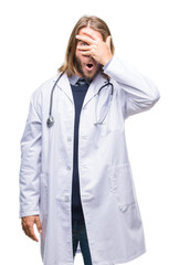 Young handsome doctor man with long hair over isolated background peeking in shock covering face and eyes with hand, looking through fingers with embarrassed expression.