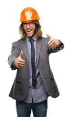 Young handsome architec man with long hair wearing safety helmet over isolated background approving doing positive gesture with hand, thumbs up smiling and happy for success. Looking at the camera