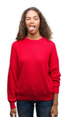 Young hispanic woman wearing red sweater sticking tongue out happy with funny expression. Emotion concept.