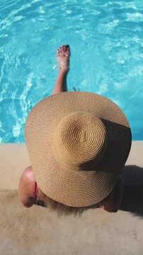 Young woman sitting in swimming pool playing with her legs. Overhead view.