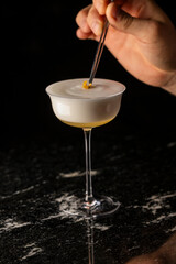 coctel en mesa negra en copa coupe y mano poniendo garnish