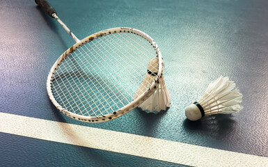 Cream white badminton shuttlecock and racket with neon light shading on floor in indoor badminton...