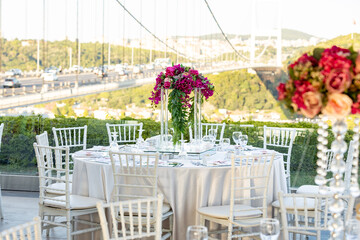 A romantic and elegant wedding reception with a breathtaking view of the Bosphorus Bridge. The tables are decorated with tall floral centerpieces and white linens