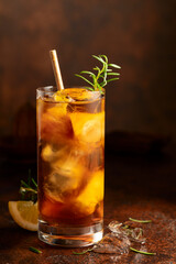 Iced tea or cocktail with ice, rosemary and lemon slices on the old brown table.