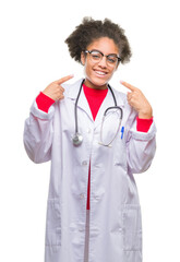 Young afro american doctor woman over isolated background smiling confident showing and pointing with fingers teeth and mouth. Health concept.