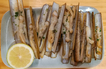 Plano superior de una exquisita ración de doce navajas a la plancha con rodaja de limón