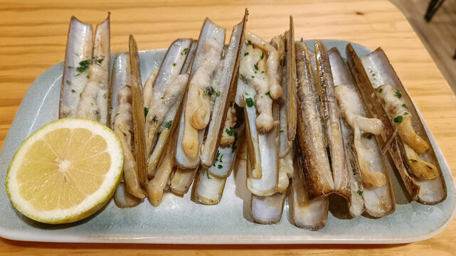 Plano oblicuo de exquisita raci&oacute;n de navajas a la plancha con rodaja de lim&oacute;n