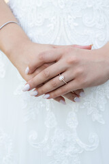 Bride's Hands with Elegant Engagement Ring in a Close-Up Shot Against a Lace Wedding Dress