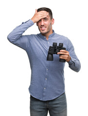 Handsome young man looking through binoculars stressed with hand on head, shocked with shame and surprise face, angry and frustrated. Fear and upset for mistake.