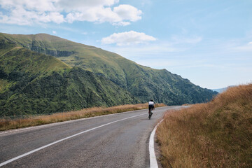Male cyclist during ride a bicycle. Sports motivation image.Good road for cycling. Man cyclist riding a gravel bike with a view of the mountains. Travel biking concept. Transfăgărășan road in Romania.