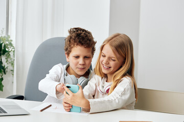 Happy Caucasian boy and girl studying at home using a laptop and headphones They are engaged in online elearning, typing and playing educational games The siblings are sitting at a table in their cozy