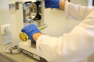 Scientist Pouring Liquid in Laboratory: A researcher in a white coat and blue gloves carefully pouring a yellow liquid from a flask onto laboratory equipment, symbolizing scientific experiment