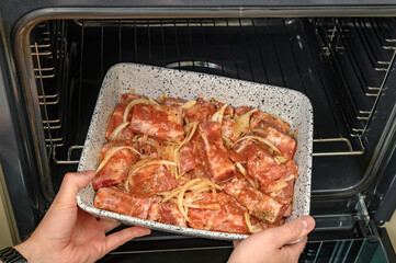 Kucharz wkłada do piekarnika domowego surowe żeberka wieprzowe w sosie barbecue