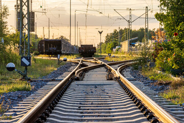 Ein Gleisbereich in einem Rangierbahnhof bei Sonnenuntergang. Mehrere Gleise laufen zusammen und...