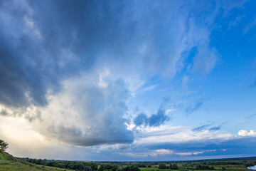 A breathtaking view unfolds with dark clouds contrasting against a vibrant sky, as the sun sets over a peaceful countryside.