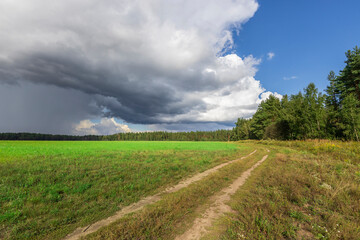 Fototapeta premium A field with a road running through it and a storm in the distance