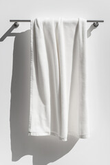 A white towel hanging, casting soft shadows, isolated on a white background, with an elegant and clean design, perfect for bathroom decor or spa use, selected focus

