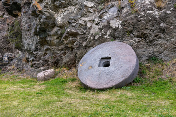 Ancient Stone Wheel and Smaller Artifact Beside Rocky Outcrop in Historical Site