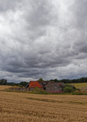 An abandoned Stone Farmhouse with attached barns in a small hollow set amongst the Farm Fields of Greenden under dark rain clouds.