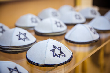 Collection of Kippahs with Star of David: Rows of white kippahs (yarmulkes) adorned with the blue Star of David, displayed for sale or use in a Jewish religious context, symbolizing faith