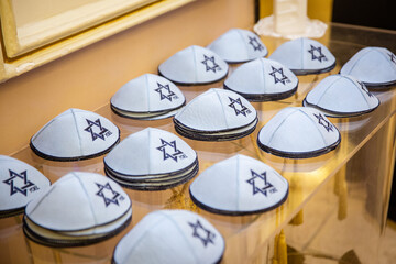 Collection of Kippahs with Star of David: Rows of white kippahs (yarmulkes) adorned with the blue Star of David, displayed for sale or use in a Jewish religious context, symbolizing faith
